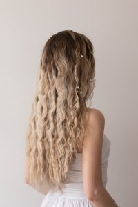 Easy summer hairstyle with soft waves and tiny white flowers woven throughout long, crimped blonde hair.